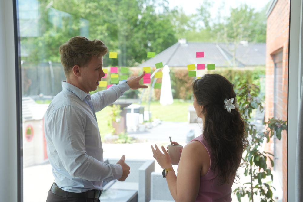 Two Juwix designers sort post-its on a window during a workshop